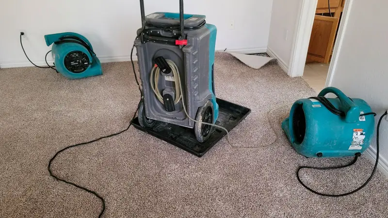Dehumidifier and two air movers running on wet carpet in an empty room